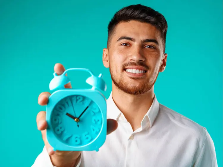 Smiling businessman holding an alarm clock, indicating set timelines for property transactions and key collection
