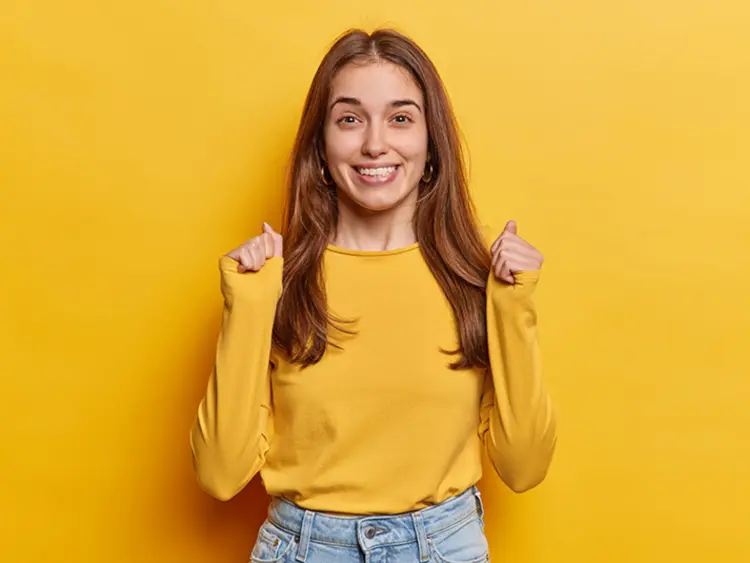 Joyful woman in yellow celebrates, symbolising the binding nature of a successful house purchase